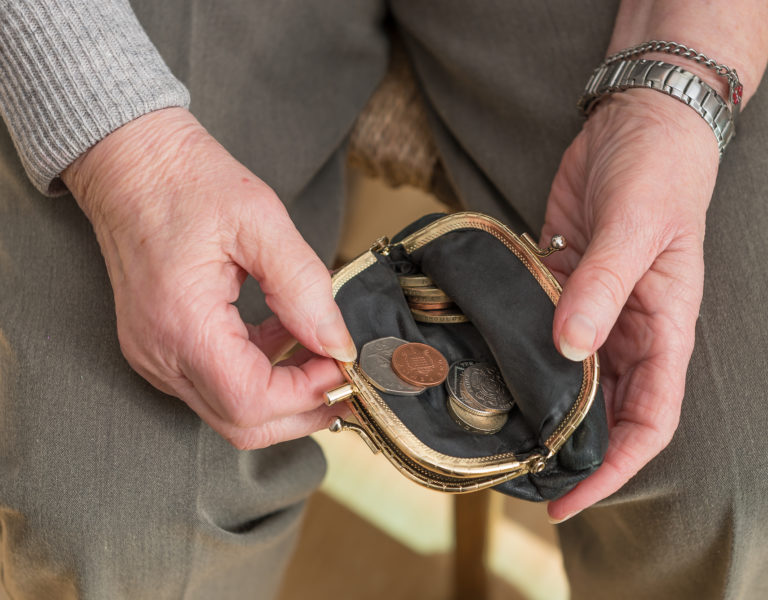 Hands of a pensioner checking her loose change in an open purse. British pounds sterling coins