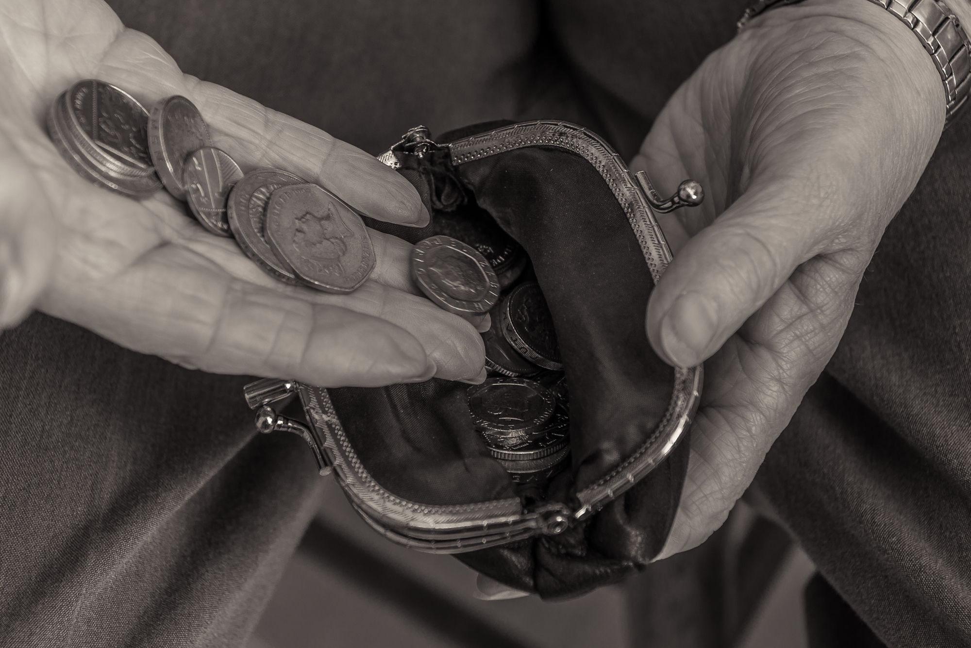 British pensioner putting coins into a purse. Close up of hands. Black and white image. Cost of living concept.