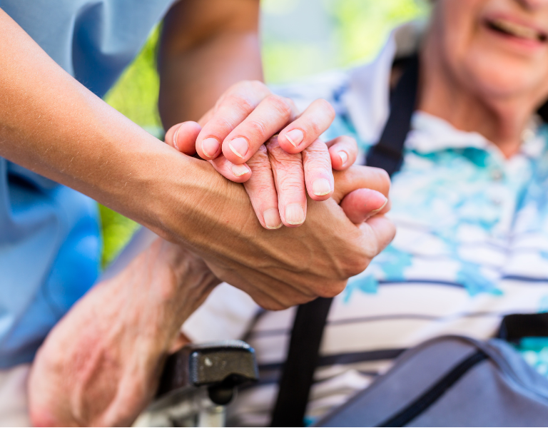 A carer and an older person holding hands