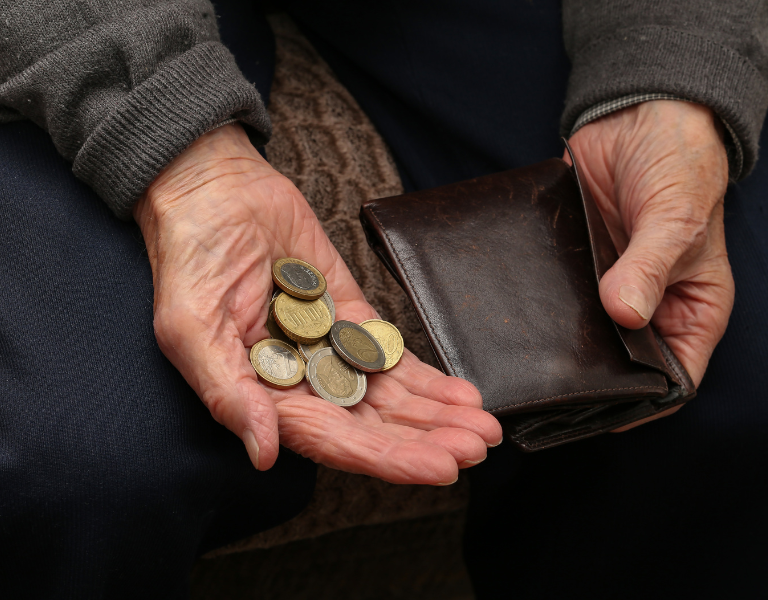A stock image showing the hands of an older man counting coins from his wallet.