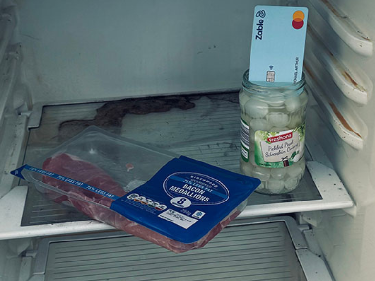 A photograph of an open fridge with very little on the shelves. Part of the Give Me Some Credit photovoice exhibition, taken by creator Michael John Arthur