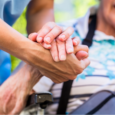 A carer and an older person holding hands